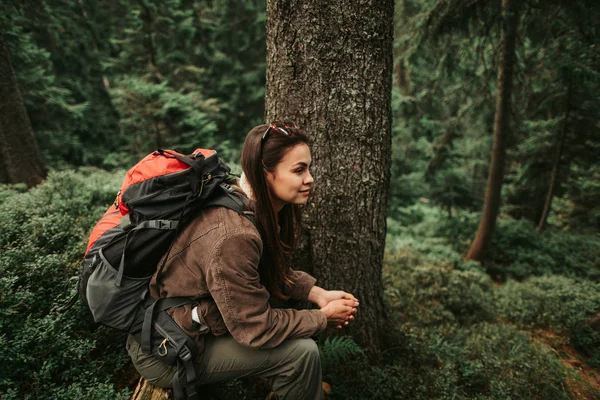 Красивая девушка с рюкзаком сидит на стволе дерева в лесу — стоковое фото