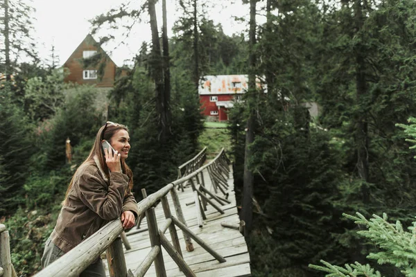 Mooie jonge vrouw praten over cellphone terwijl staande op houten voetgangersbrug — Stockfoto