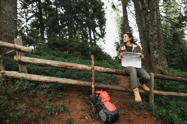 Aantrekkelijke jonge dame zittend op een houten hek en houden van de kaart — Stockfoto