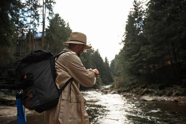 Внимательный путешественник проверяет время, находясь у реки — стоковое фото