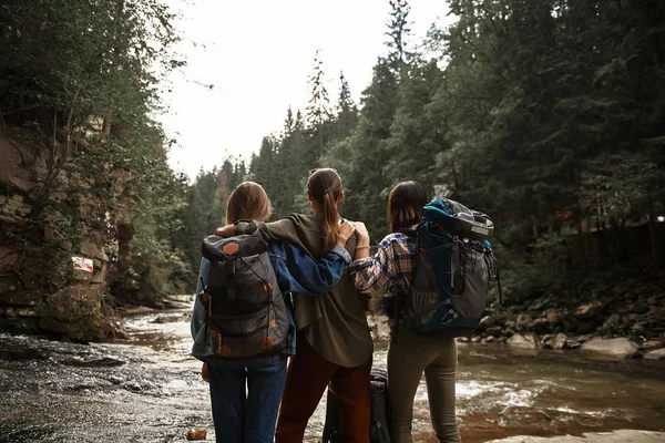 Drie jonge vrouwen permanent samen en kijken naar de bergbeek — Stockfoto