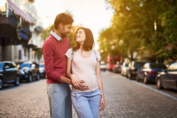 Homem barbudo feliz abraçando encantadora esposa grávida e tocando sua barriga — Fotografia de Stock