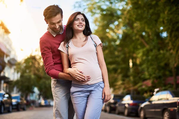 Бородатий чоловік обіймає свою красиву вагітну дружину і торкається її живота — стокове фото