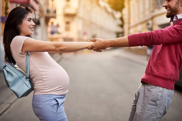 Щасливі майбутні батьки тягнуть один одного за руки на вулицю — стокове фото