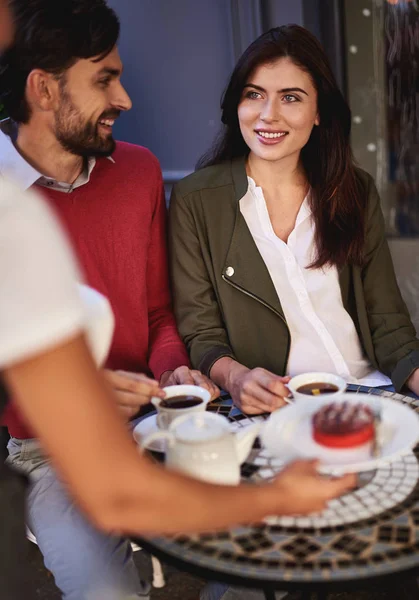 Young couple spending time in outdoor cafe while waitress serving cake — Stock Photo, Image