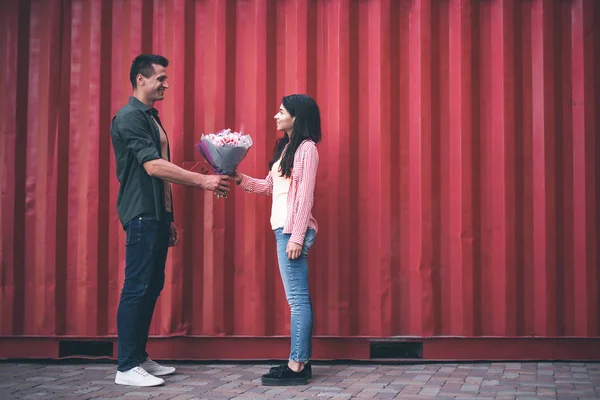 Bello uomo in piedi di fronte a giovane donna e dando i suoi fiori — Foto Stock