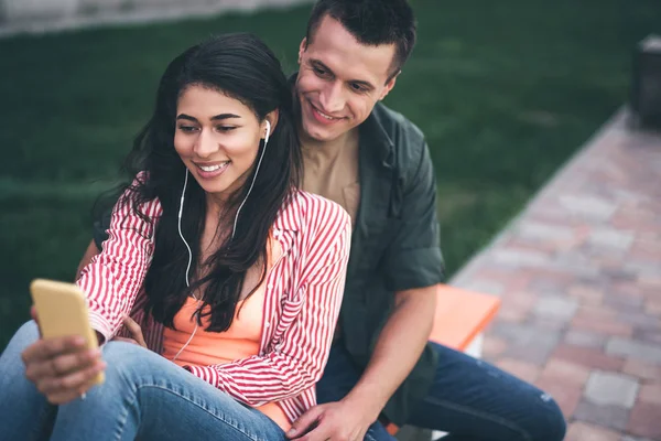 Hombre sonriente mirando la pantalla mientras su novia escucha música — Foto de Stock