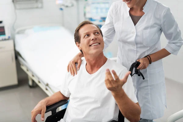 Hombre en silla de ruedas mirando a la enfermera con sonrisa — Foto de Stock