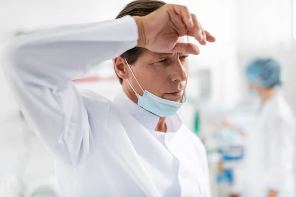Καταπονημένος γιατρός με προστατευτική μάσκα στο πηγούνι του να αγγίζει το μέτωπο — Φωτογραφία Αρχείου