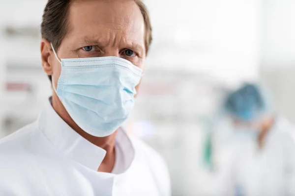 Médico en máscara protectora de pie en la habitación del hospital sobre fondo borroso — Foto de Stock