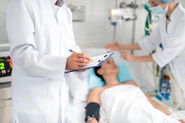 Médico llenando formulario médico mientras enfermera poniendo máscara de oxígeno en el paciente — Foto de Stock