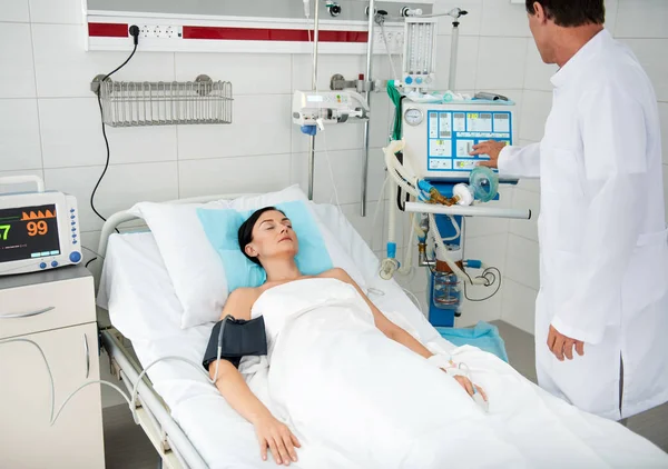 Médico masculino verificando máquina de respiração enquanto jovem senhora dormindo — Fotografia de Stock