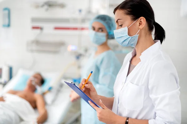 Vrouwelijke arts opvullen van medisch formulier tijdens het kijken naar haar verpleegkundige — Stockfoto