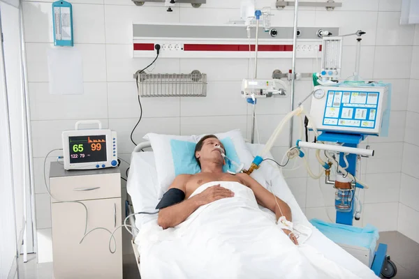 Paciente deitado na cama do hospital, rodeado por equipamentos médicos — Fotografia de Stock