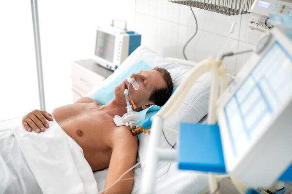 Unconscious patient on mechanical ventilator lying in hospital bed