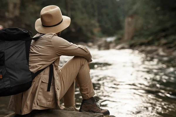 Уставший путешественник задумчиво смотрит на реку, сидя — стоковое фото