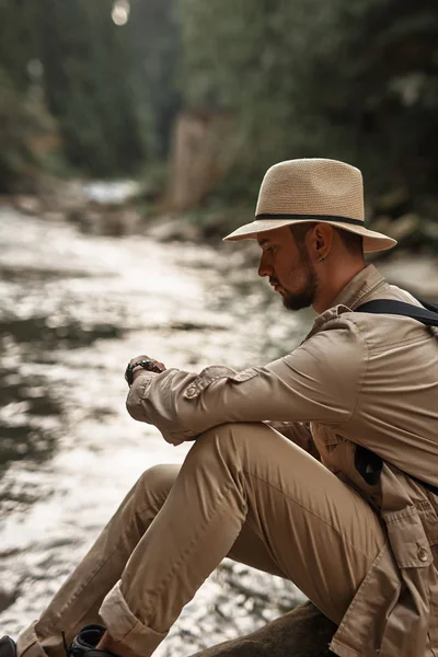 Kalm reiziger zijn horloge kijken terwijl u zit in de buurt van de rivier — Stockfoto