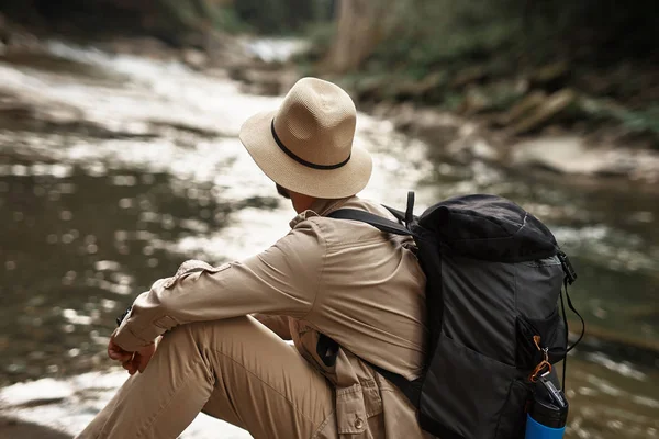 Крупный план молодого человека, сидящего и смотрящего на реку — стоковое фото