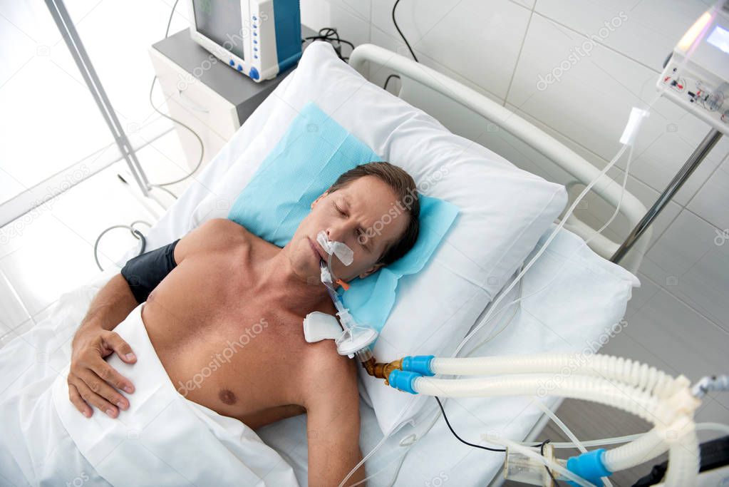 Middle aged man on breathing machine sleeping in hospital bed after surgery