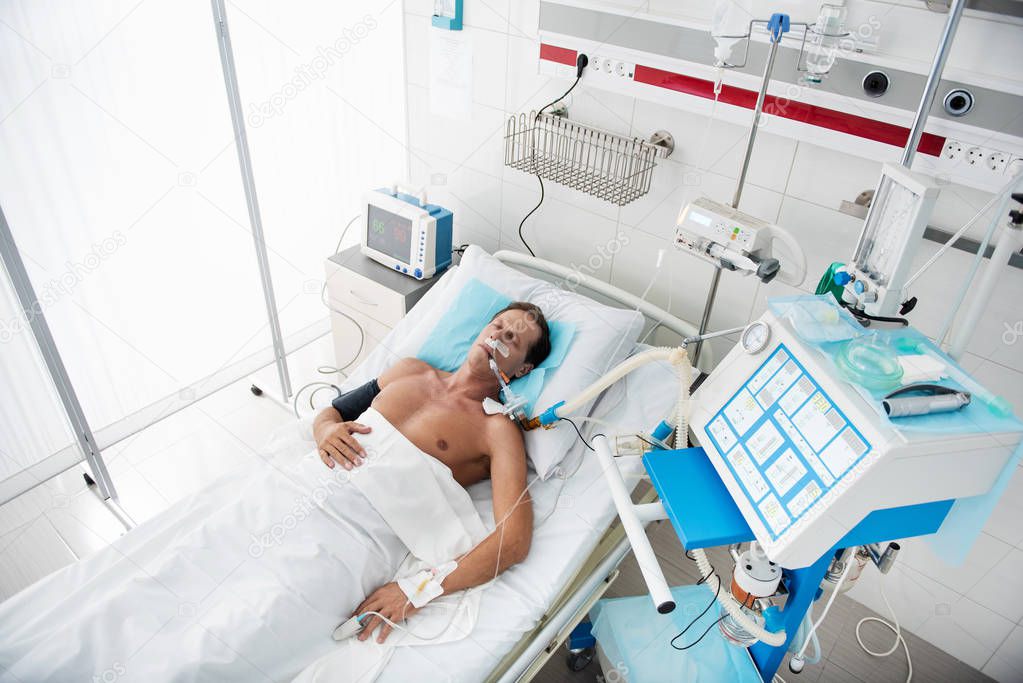 Middle aged man resting in hospital bed surrounded by medical equipment