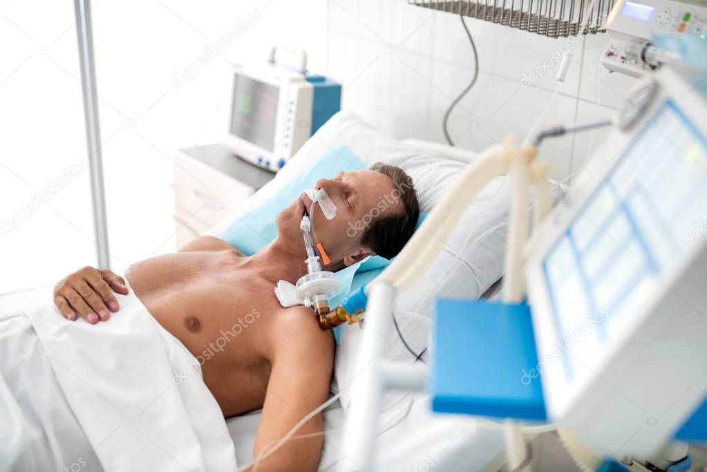 Unconscious patient on mechanical ventilator lying in hospital bed