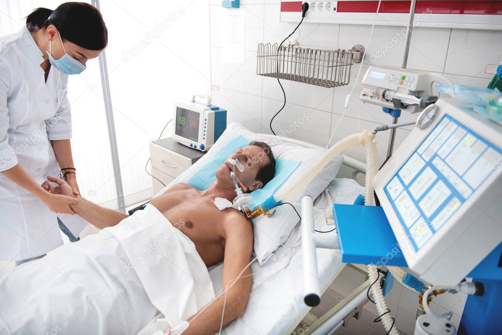 Nurse checking pulse of critical patient on breathing machine