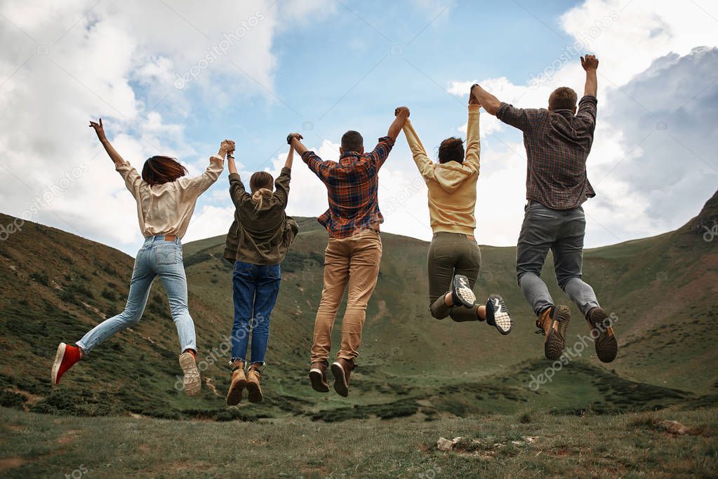 Excited friends holding hands and jumping while being in the mountains