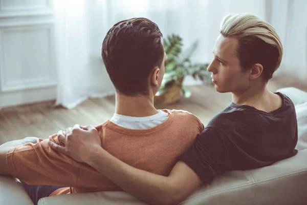 Pareja gay abrazándose y mirándose mientras están sentados en el sofá — Foto de Stock