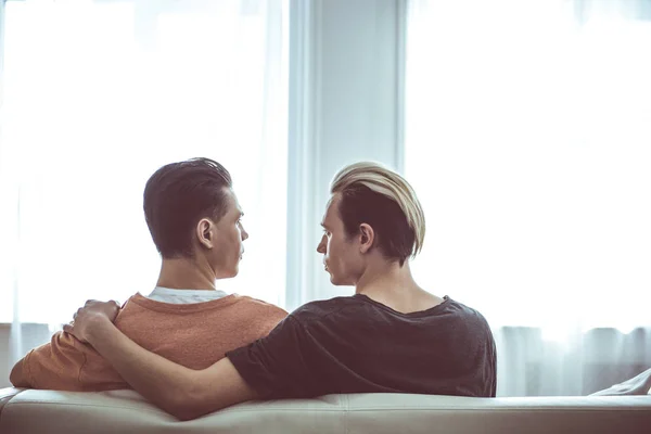 Pareja gay mirando el uno al otro mientras sentado en sofá — Foto de Stock