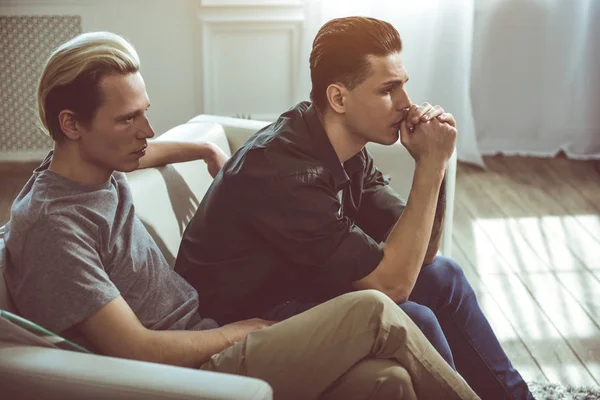 Två unga allvarliga män sitter på soffan hemma — Stockfoto
