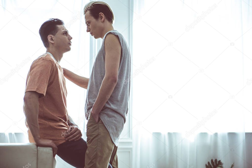 Young gay couple looking at each other at home