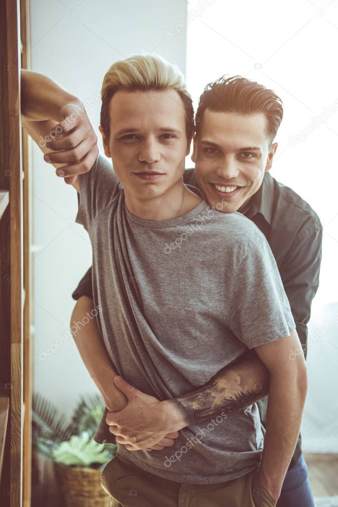 Happy gay couple hugging and looking at camera with smiles