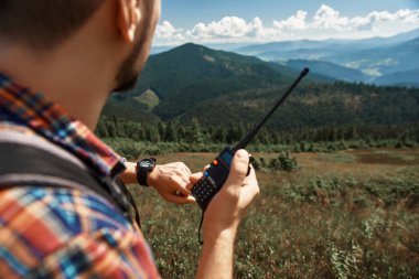 Man is using watch and radio in mountains clipart