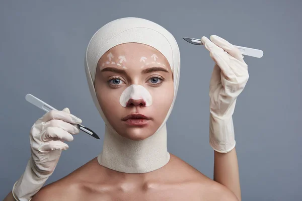 Mulher séria com ligaduras na cabeça sendo cercada por bisturis — Fotografia de Stock