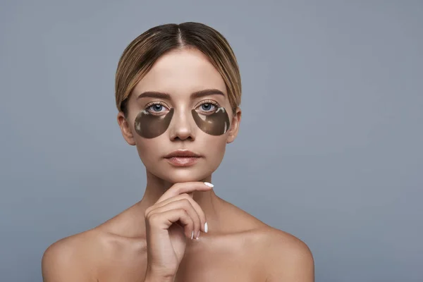 Doordachte dame gelet hand in de buurt van haar kin en met behulp van eye patches — Stockfoto