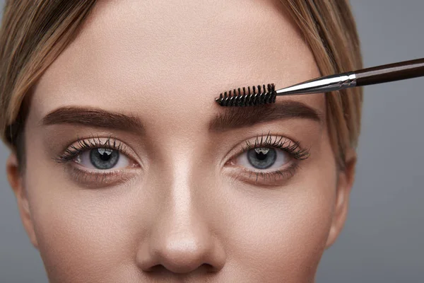 Nahaufnahme der Augen einer jungen Frau mit Pinsel auf den Augenbrauen — Stockfoto