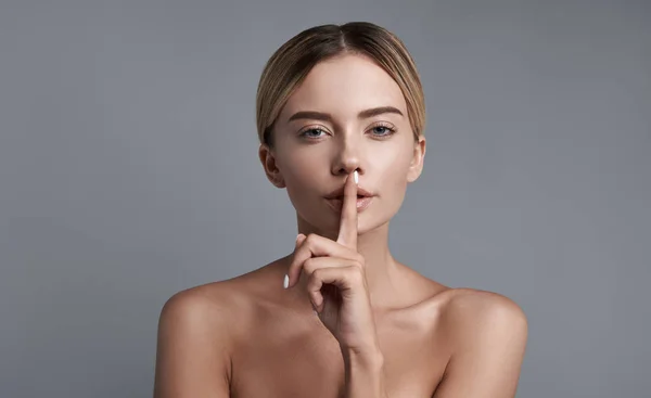 Junge Frau legt den Finger auf die Lippen und bewahrt Geheimnisse — Stockfoto