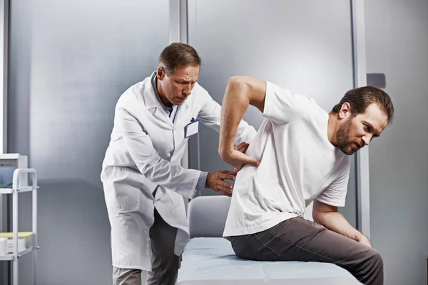 慎重に若い男の裏を検査し 痛みの中心を探して医療顧問 — ストック写真