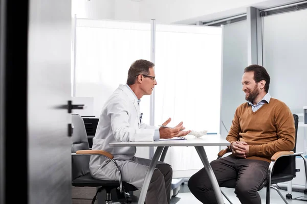 Volwassen arts in gesprek met de patiënt in lichte kantoor — Stockfoto
