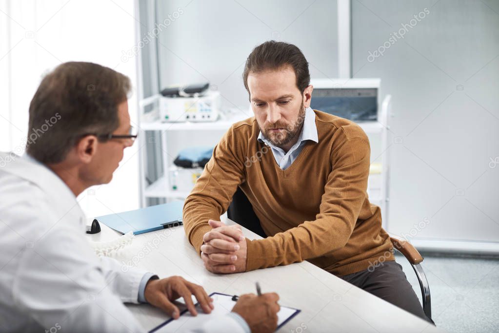 Medical adviser consulting male patient in cabinet