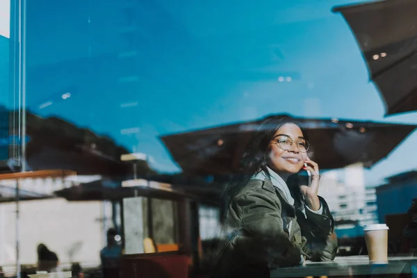 Positive lady talking on the phone while sitting in the cafe