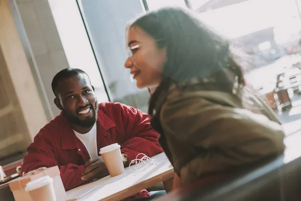 Hombre barbudo sentado en el café y sonriendo mientras mira a su novia —  Fotos de Stock