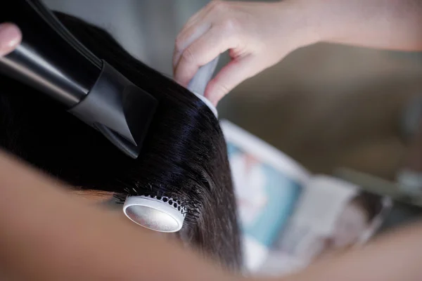 丸いブラシで行われている女性の髪の毛のトップ ビューに焦点を当てます スタイリストは 装置とドライヤーを固定するために保持しています — ストック写真