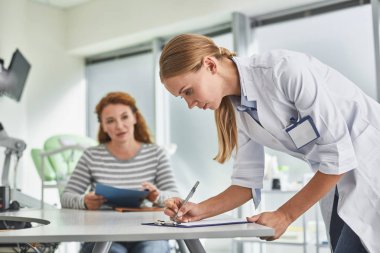 Genç doktor masada otururken hasta tıbbi formu doldurarak