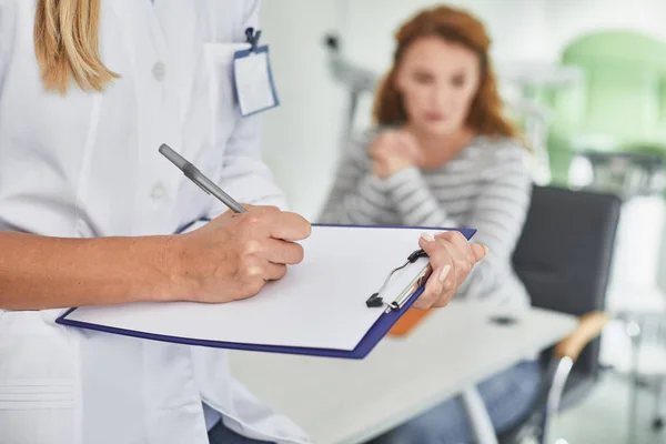 Jovem ginecologista preenchendo formulário médico enquanto o paciente espera — Fotografia de Stock