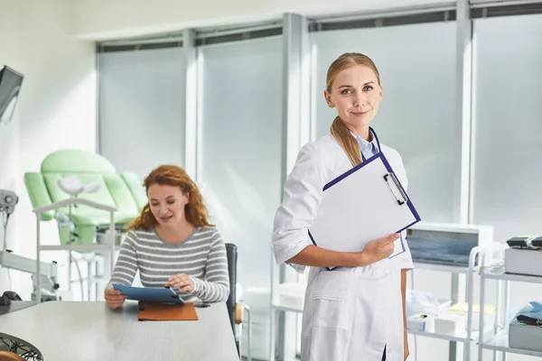 Joven médico posando en gabinete ginecológico con portapapeles — Foto de Stock
