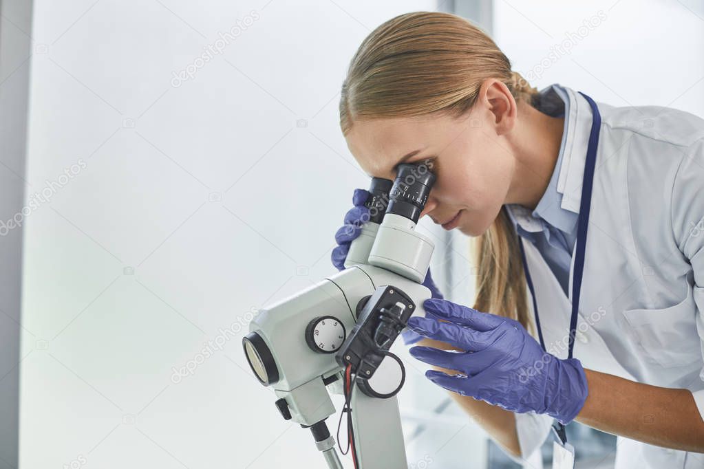 Young doctor looking through colposcope at laboratory