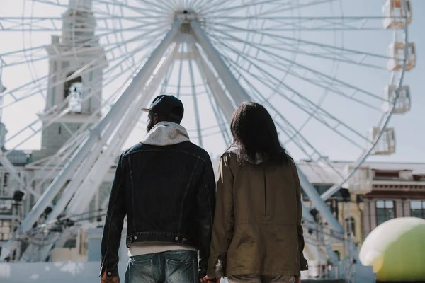 Visão traseira de um jovem casal em pé perto da roda gigante — Fotografia de Stock