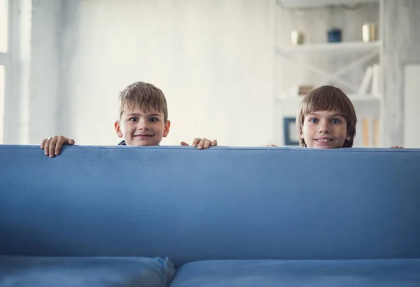 Divertenti ragazzi sorridenti mentre si nascondono dietro il divano a casa — Foto Stock