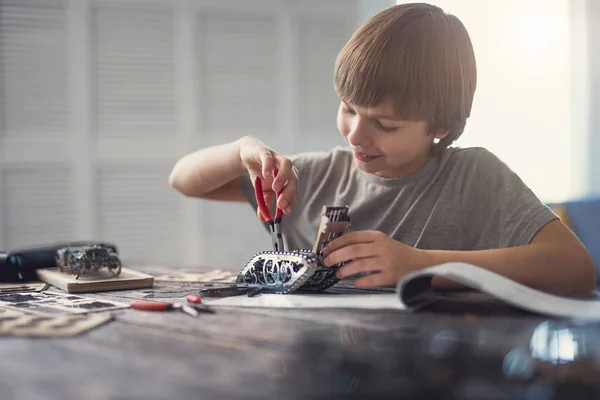 Positieve jongen glimlachen terwijl het gebruiken van tangen in zijn werk met mechanismen — Stockfoto